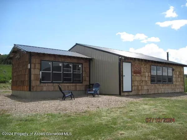 Low single-story building with brown shingle siding, a metal roof, and two blue chairs outside.