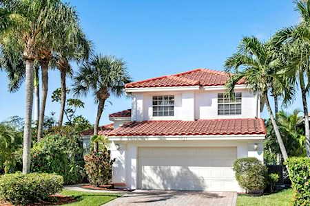 Two-story white home with a red tile roof, double garage, and palm-lined driveway.