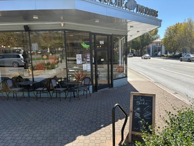 Café storefront with outdoor tables and a sidewalk chalkboard beside a sunny street.
