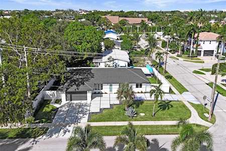 Aerial view of a single-story home with a palm-lined lawn and turquoise backyard pool.