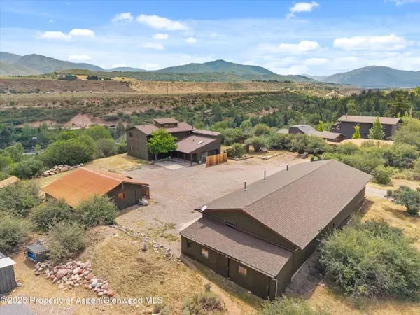 Several buildings on a rural property, with trees and distant mountains.