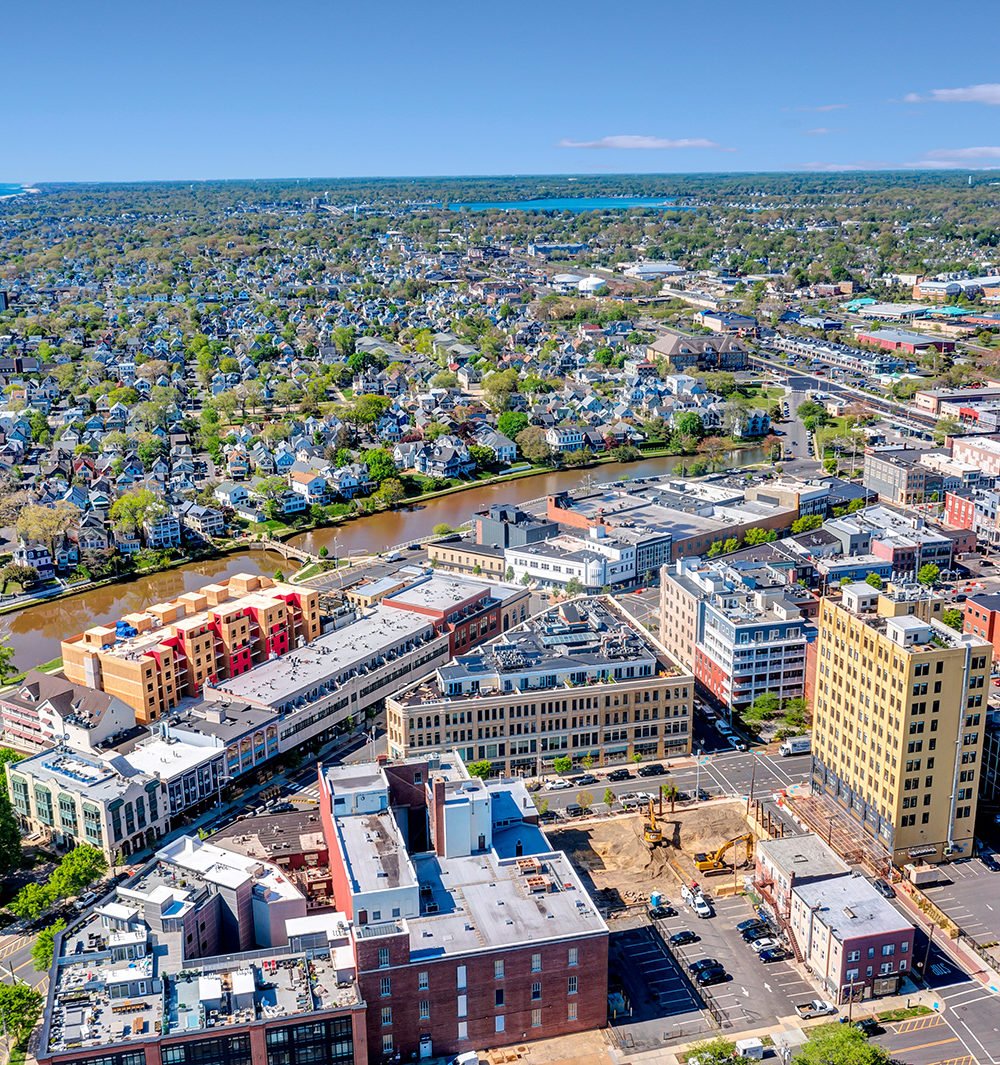 Aerial city view with a construction site in the foreground and a river winding through residential blocks.
