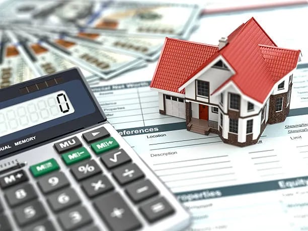 Model house, calculator, and financial paperwork arranged to illustrate home-buying costs.