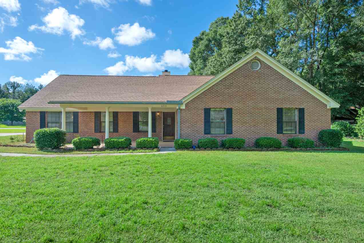 A brick home surrounded by a spacious yard featuring lush green grass.