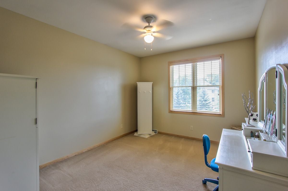 Carpeted bedroom with a window, ceiling fan, and white vanity beside a blue chair.