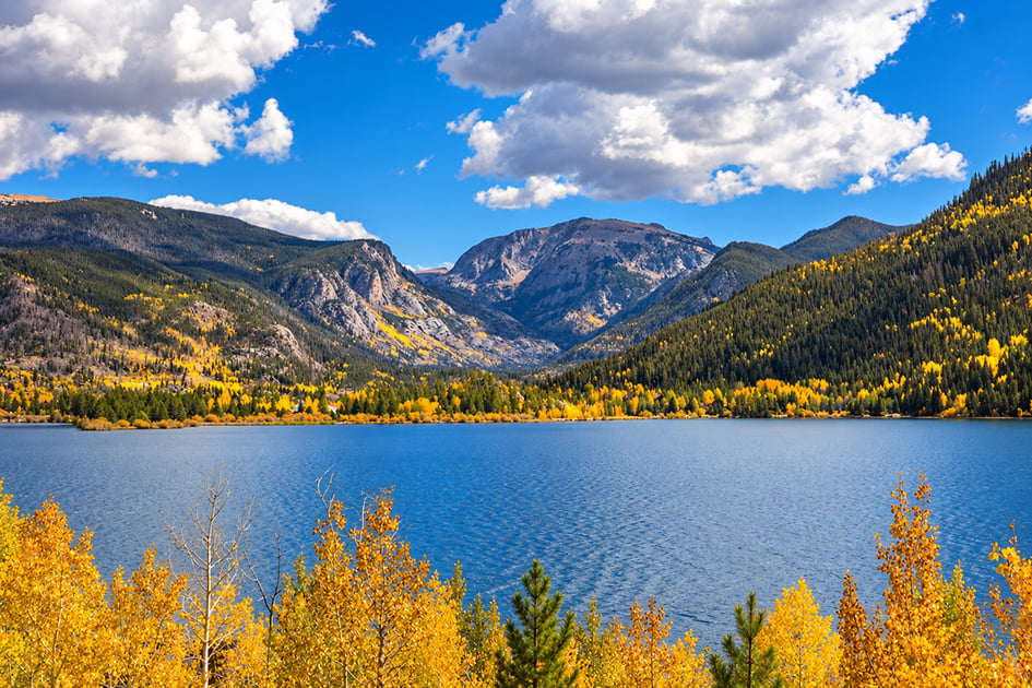 Alpine lake below mountain slopes covered in golden autumn aspens.