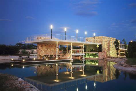 Modern stone residence illuminated at night, reflected in a surrounding lagoon.