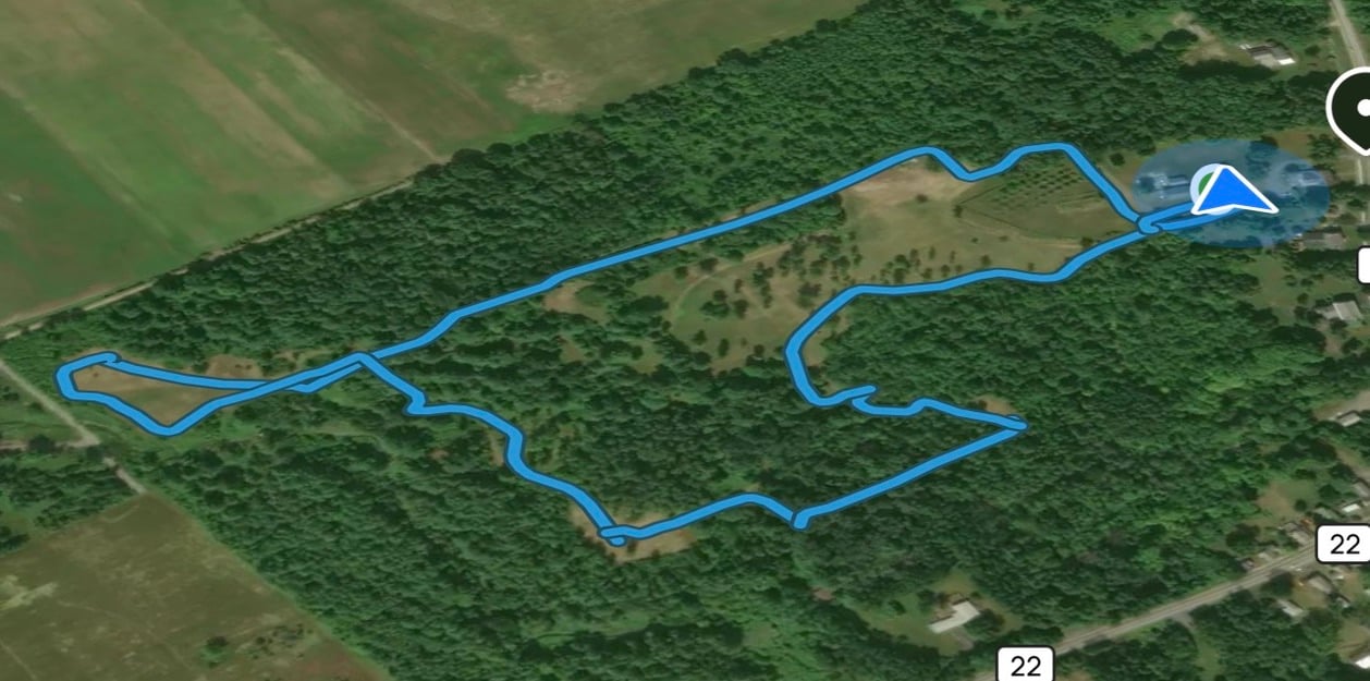 A blue trail route loops through wooded areas and open fields on an aerial map.