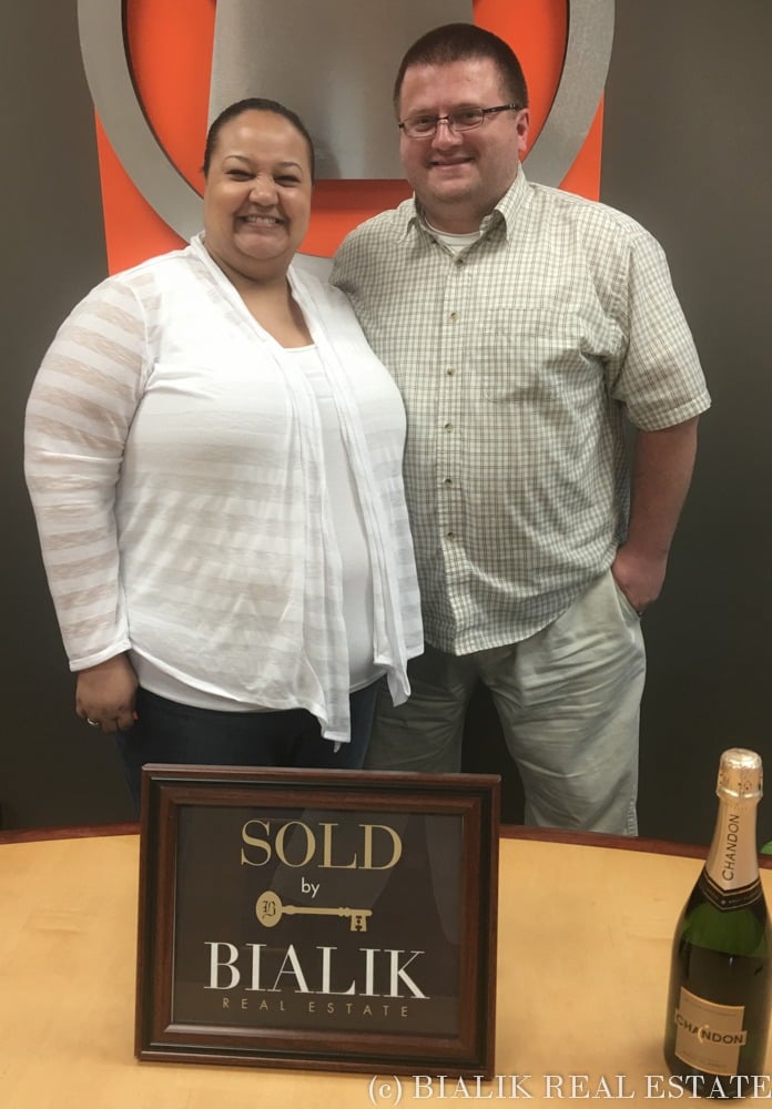 Chase and Andrea pose beside a Bialik Real Estate sold sign and champagne.