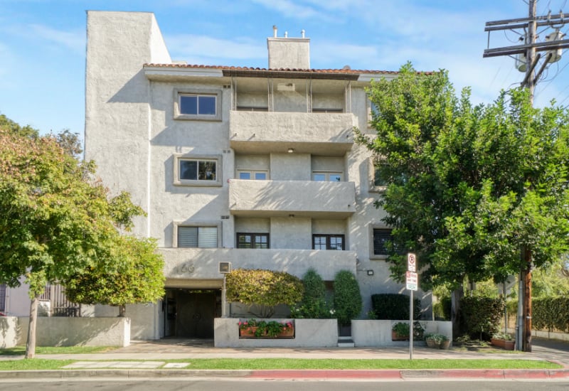 Apartment building with pale stucco facade, stacked balconies, and landscaped street frontage.