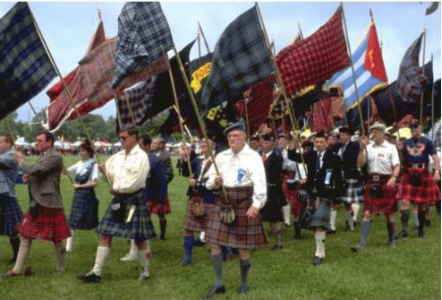 Men in kilts gather beneath tartan flags at an outdoor Highland event.