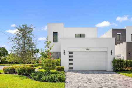 Modern white house with a wide garage, stone driveway, and landscaped front lawn.