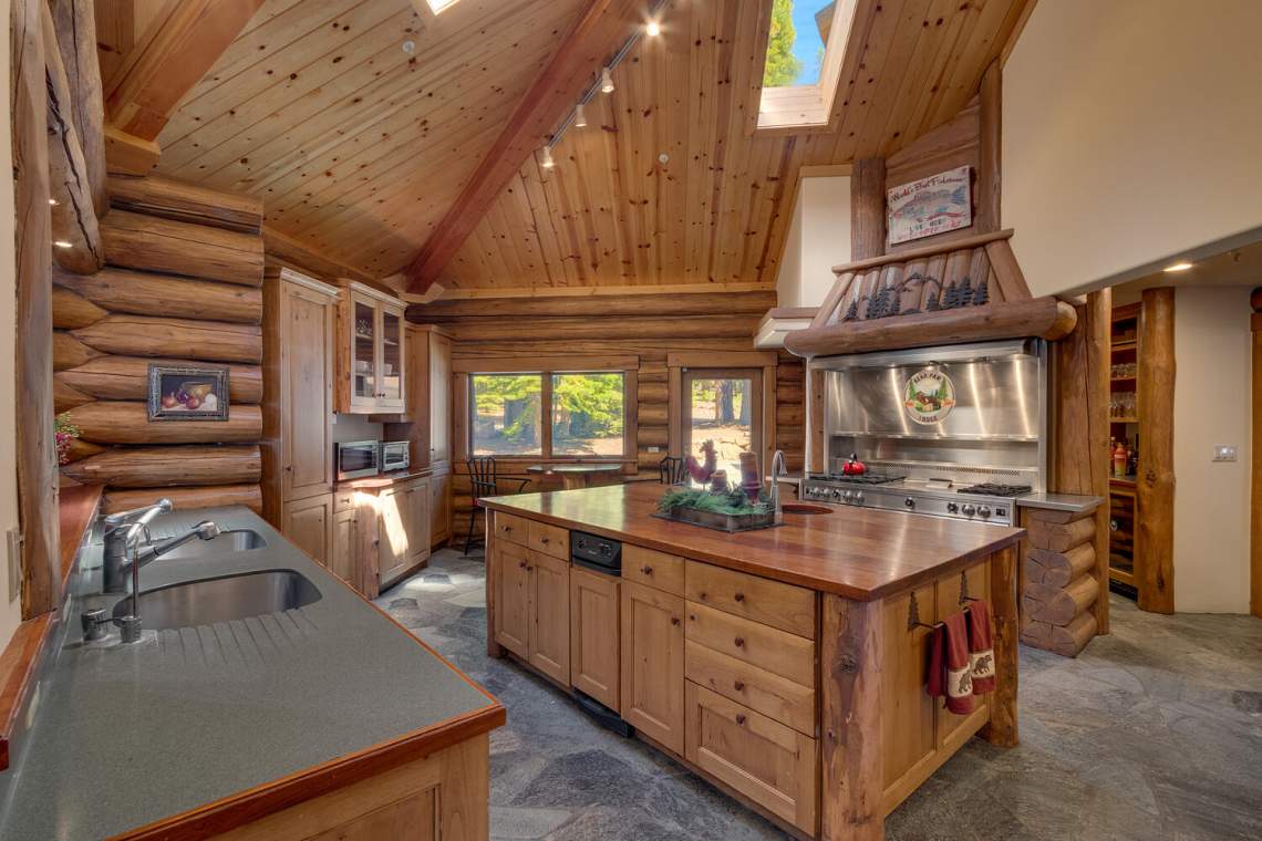 Rustic log-cabin kitchen with a large wooden island, stainless-steel range, and skylight.