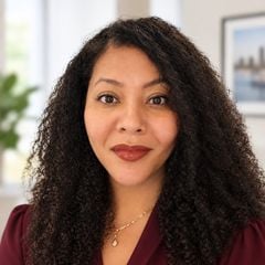 Marissa Amin with long curly dark hair, wearing a burgundy top and gold necklace.