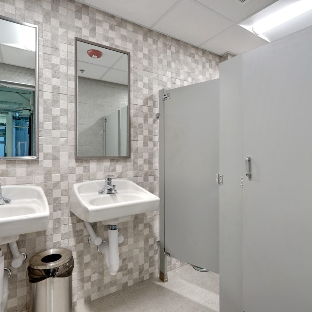 Restroom with patterned gray tile walls, wall-mounted sinks, mirrors, and gray stall partitions.