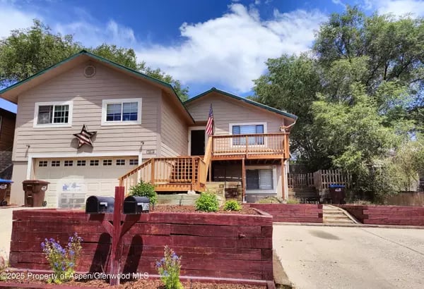 Beige two-story home with an attached garage, wooden decks, and an American flag.