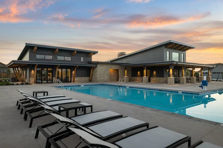 Community pool beside a modern clubhouse at sunset, with rows of lounge chairs.