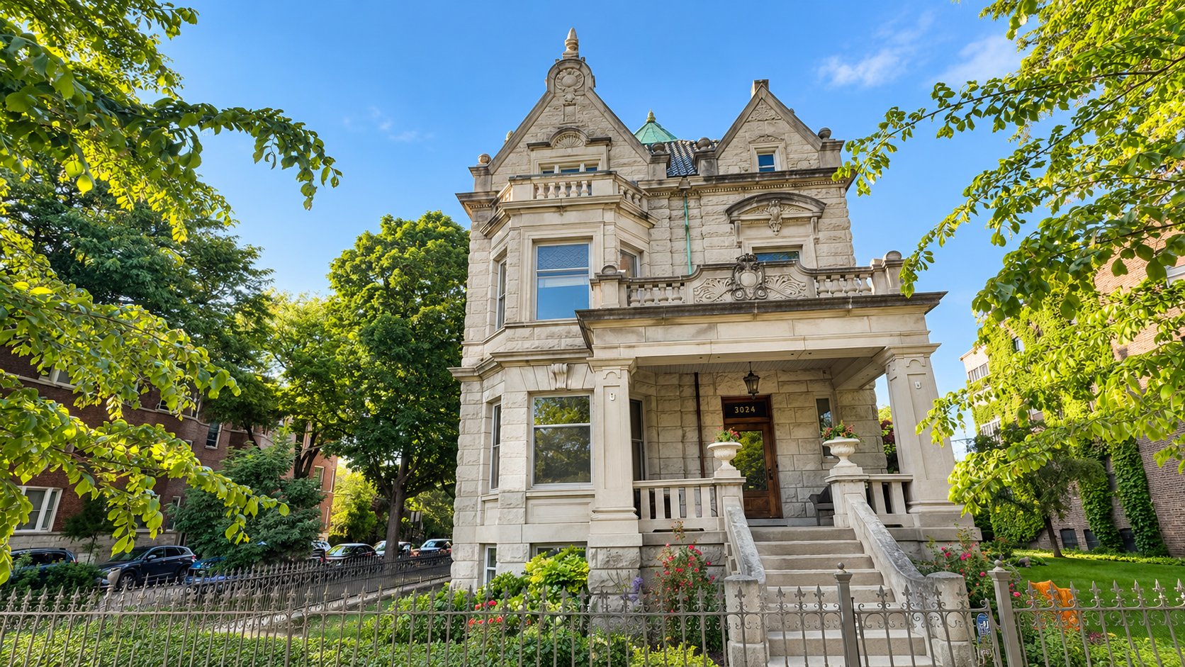 Ornate limestone residence with a clock tower, broad porch, and iron front fence.