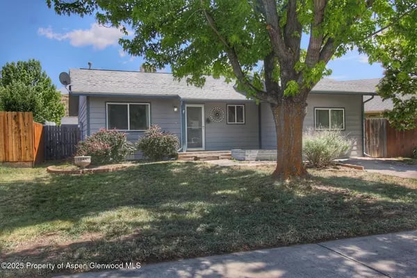 Single-story blue-gray house behind a large shade tree and front lawn.