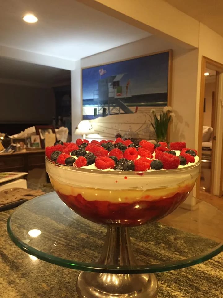 Berry-topped holiday trifle layered with custard and red fruit in a glass pedestal bowl