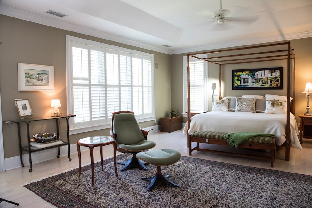 Master bedroom with a four-poster bed, shuttered windows, and green lounge chair.