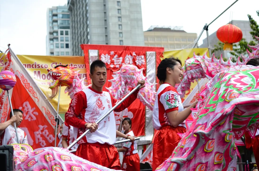 Performers in traditional attire holding a large pink dragon during a dragon dance at the San Francisco Autumn Moon Festival.