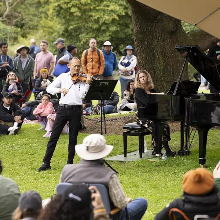 San Francisco Symphony musicians performing violin and piano duet outdoors with diverse audience sitting on law