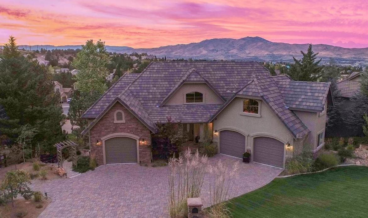 Perched above Reno behind the gates of Mountainshyre in the Caughlin Ranch community, 4905 Mountainshyre Road offers a lifestyle of elegance, security, and comfort. Completed in 2013, this 3904 sqft. custom home spans three levels and blends timeless architecture with modern conveniences, all while showcasing breathtaking views of the city skyline and surrounding mountains.  You're instantly welcomed by the home's lush curb appeal, with its paver driveway that leads to the stone-accented exterior, fresh stucco finish, and quartzite steps, making a striking first impression. Inside, a travertine foyer welcomes you to soaring ceilings and windows that frame the panoramic views.