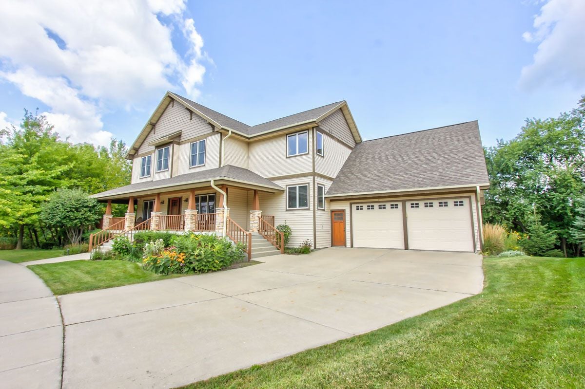 Two-story beige home with a covered porch, flower beds, and an attached two-car garage.
