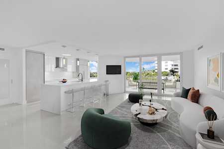 Modern open-plan living room with a white curved sofa, green chair, and balcony doors.