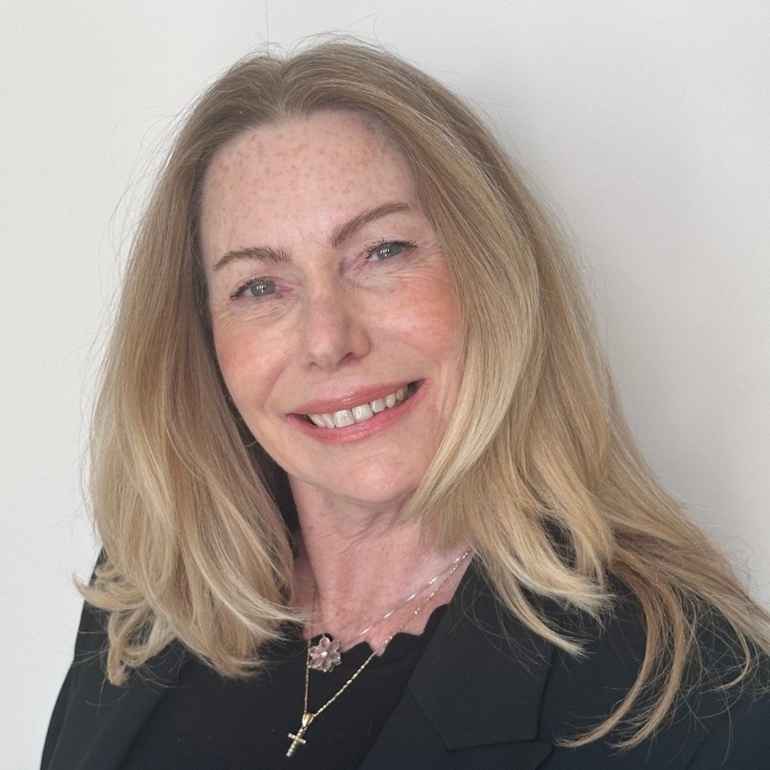 Caroline McCabe smiling in a black blazer and layered necklaces.