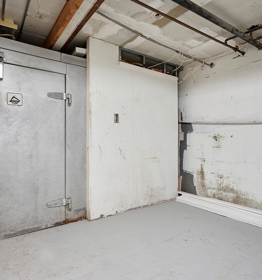 Unfinished utility room with a metal door, white partition, exposed beams, and masonry walls.