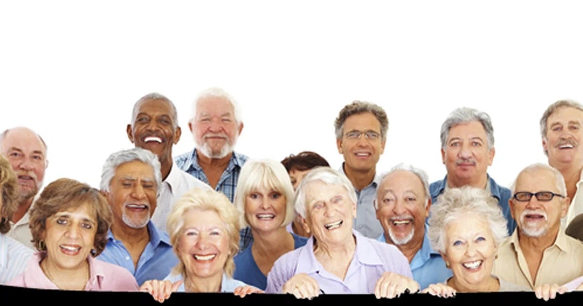 A smiling group of older adults standing close together against a white background.