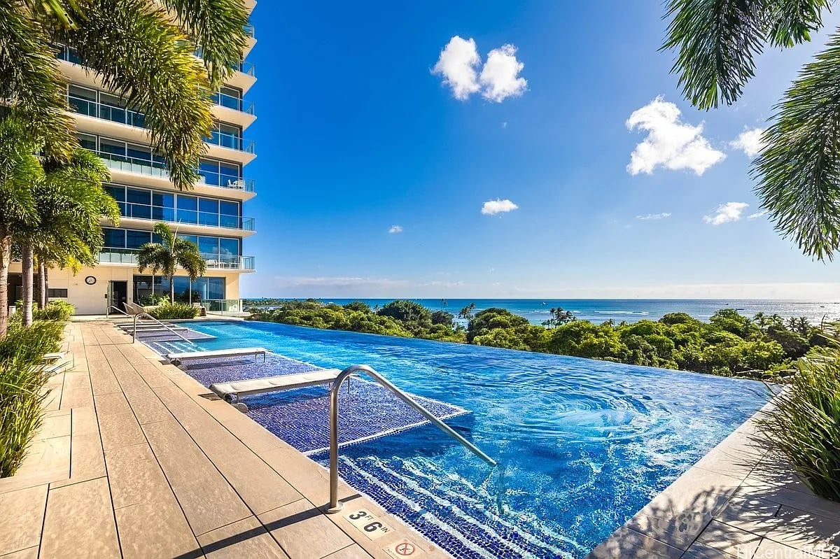 Condominium infinity pool overlooking the ocean, framed by palm trees and a landscaped terrace.
