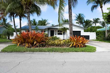 Modern white home framed by tall palms and colorful tropical landscaping.