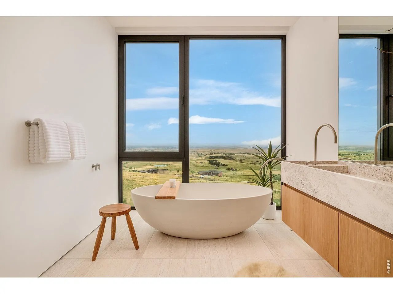 Modern bathroom with a freestanding tub and expansive windows overlooking open countryside.