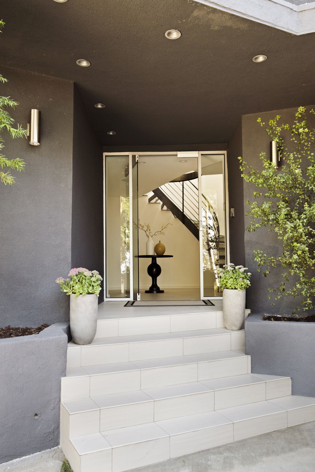 Modern home entrance with white tiled steps, glass doors, and potted plants.