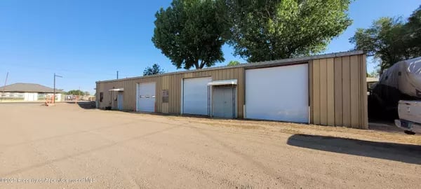 Tan metal garage building with multiple doors and a broad gravel lot.