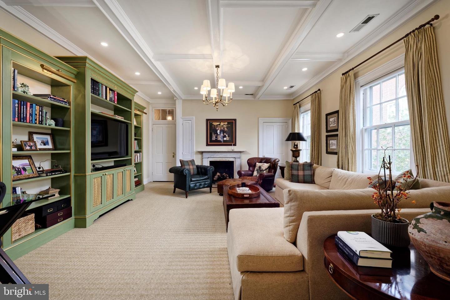 Living room with green built-in bookshelves, a fireplace, coffered ceiling, and large windows.