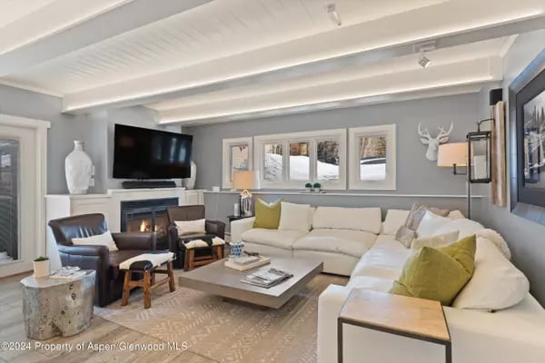 Furnished living room with a white sectional, green accent pillows, and exposed ceiling beams.