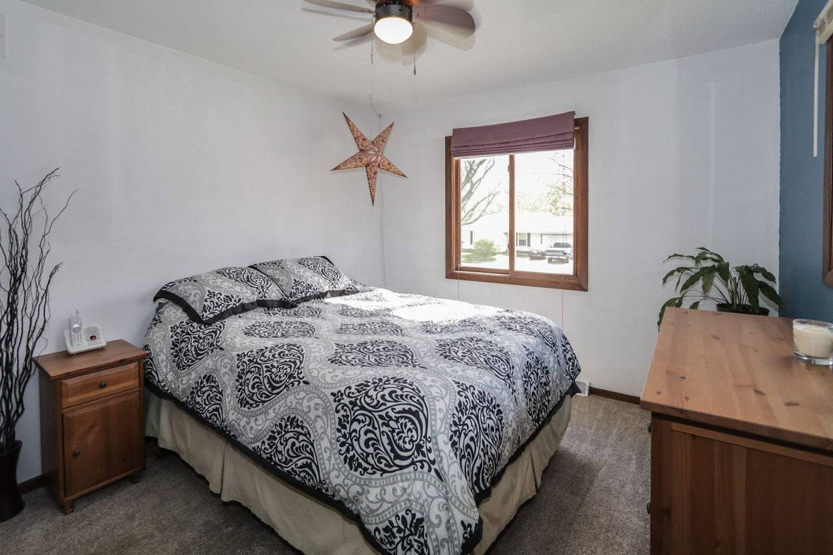 Bedroom with a black-and-white patterned bedspread, wooden furniture, and a window with a purple shade.