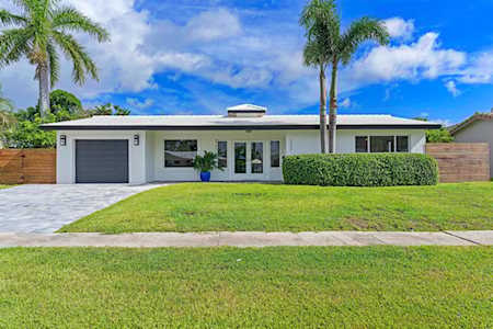 Modern single-story home with an attached garage, palm trees, and a broad green lawn.