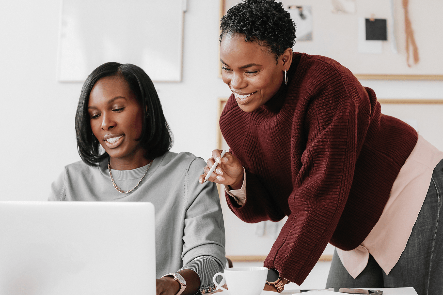 Two women review a laptop together as one points at the screen.