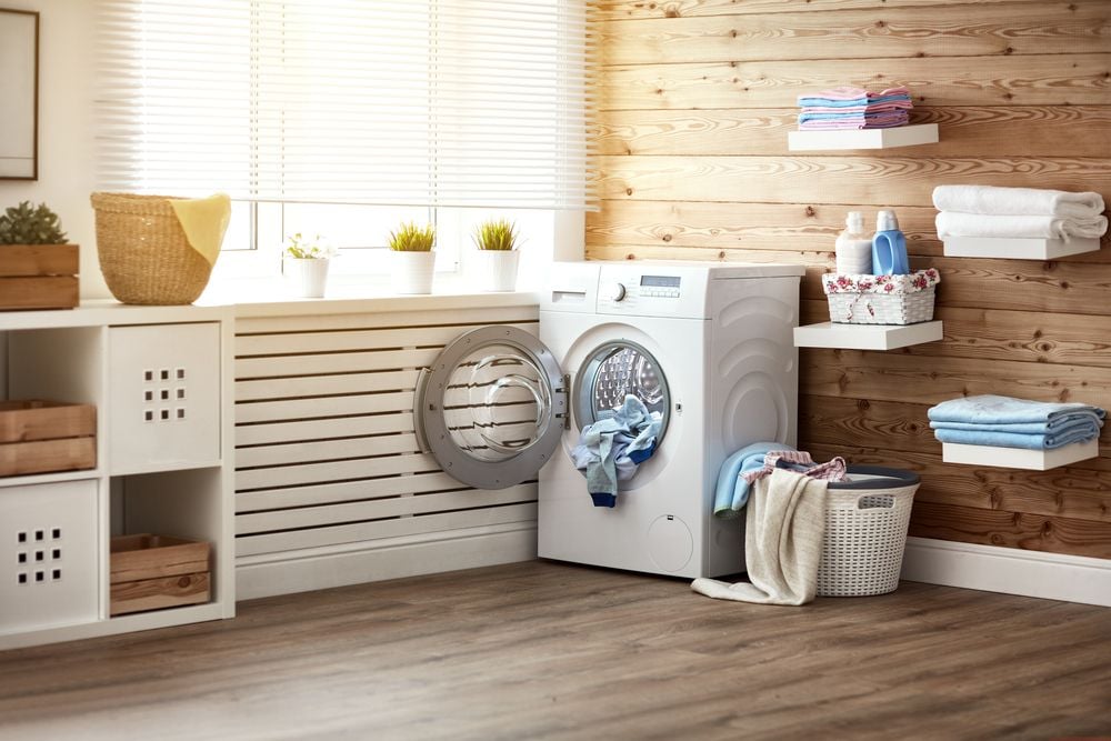 Laundry room with a front-loading washer, folded towels, and a wood plank wall.
