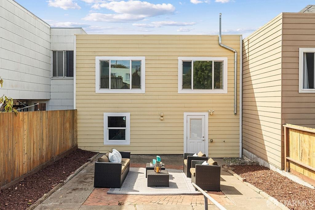 Rear exterior of a pale yellow home with a furnished paved patio and fenced side yards.
