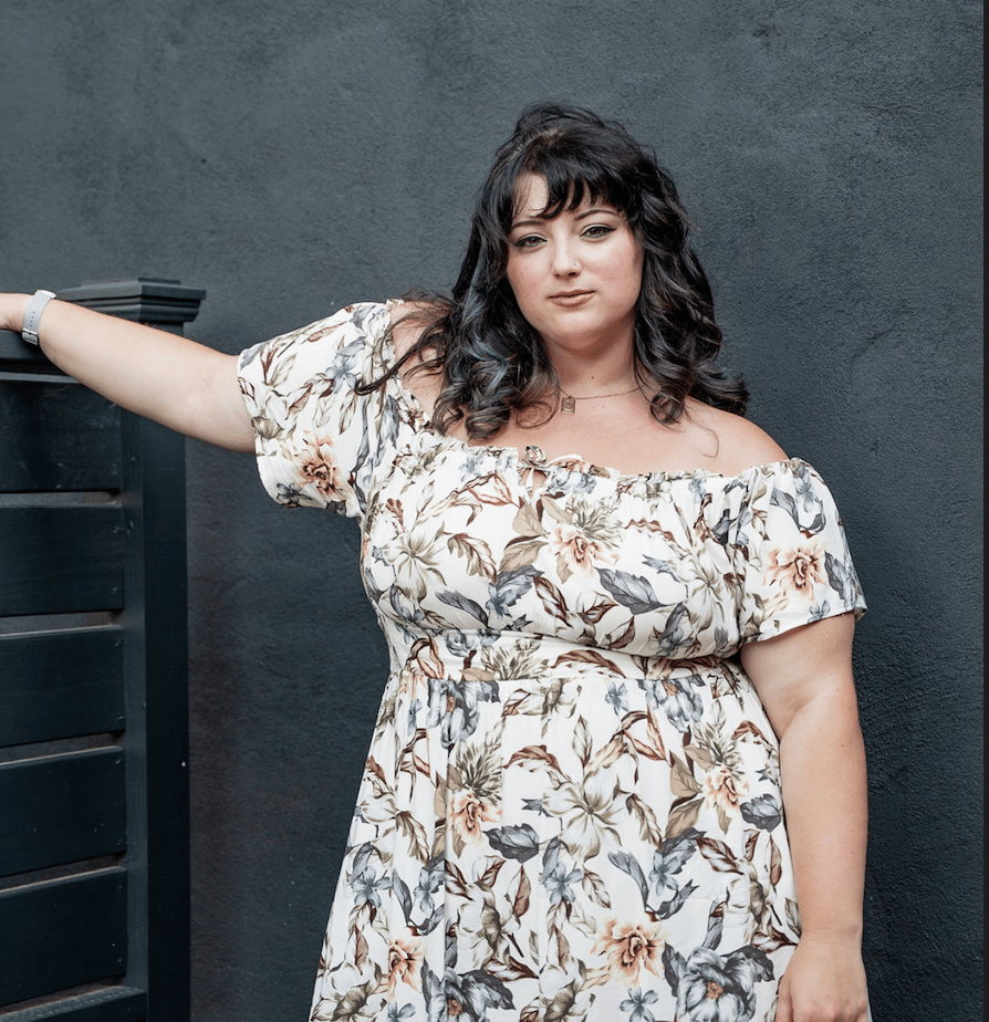 Woman in a floral dress posing beside dark stairs against a charcoal wall.