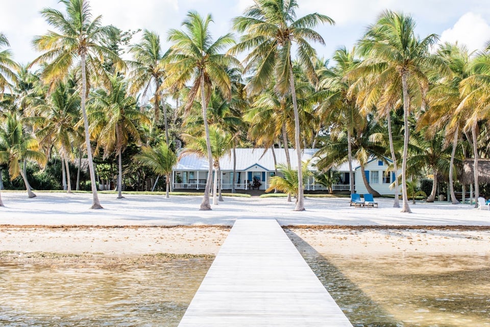 Beachfront home in Naples FL with palm trees, lounge chairs, and a private dock leading to calm Gulf waters