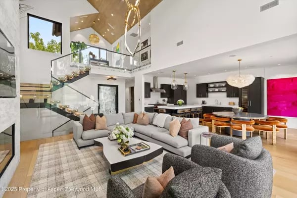 Open-plan living room with a glass-railed staircase, double-height ceiling, and adjoining modern kitchen.