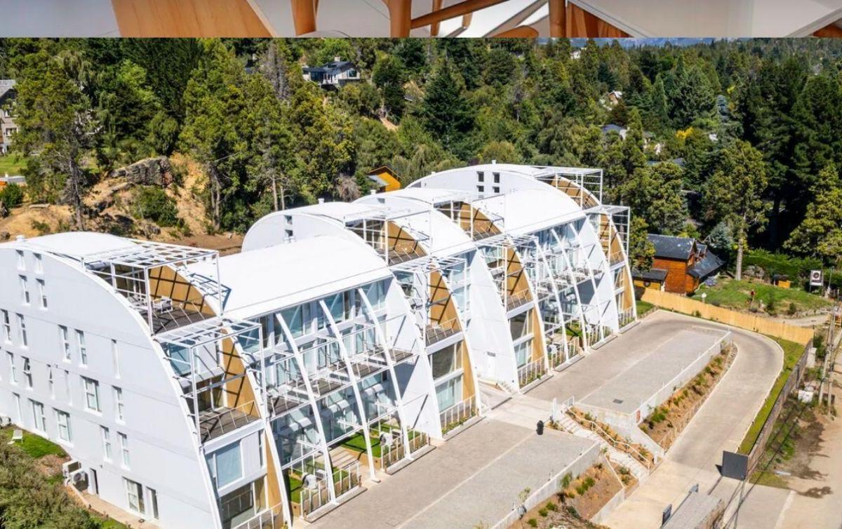 Modern white apartment complex with curved rooflines and glass balconies on a wooded hillside.