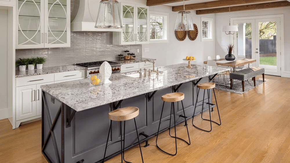 Bright kitchen with a large gray island, patterned stone countertop, and wooden bar stools.